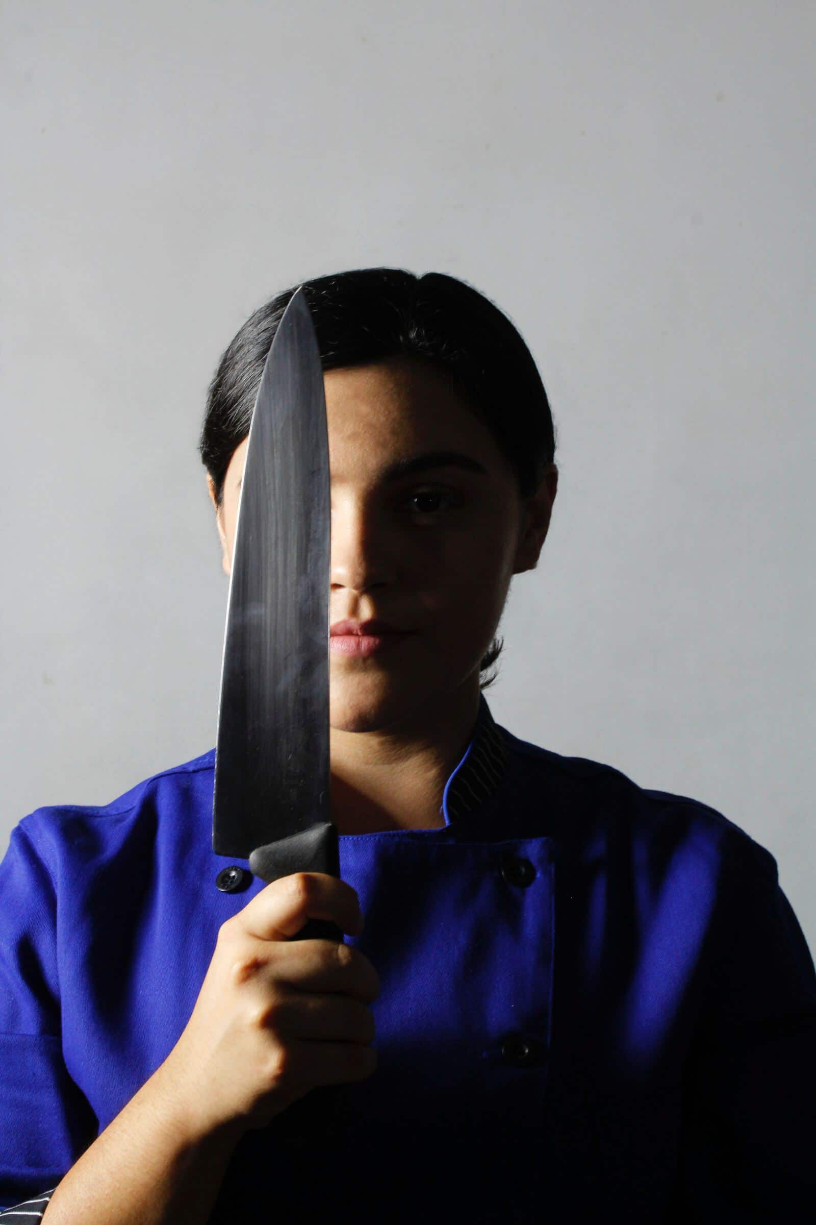 a chef hiding half of her face using a knife