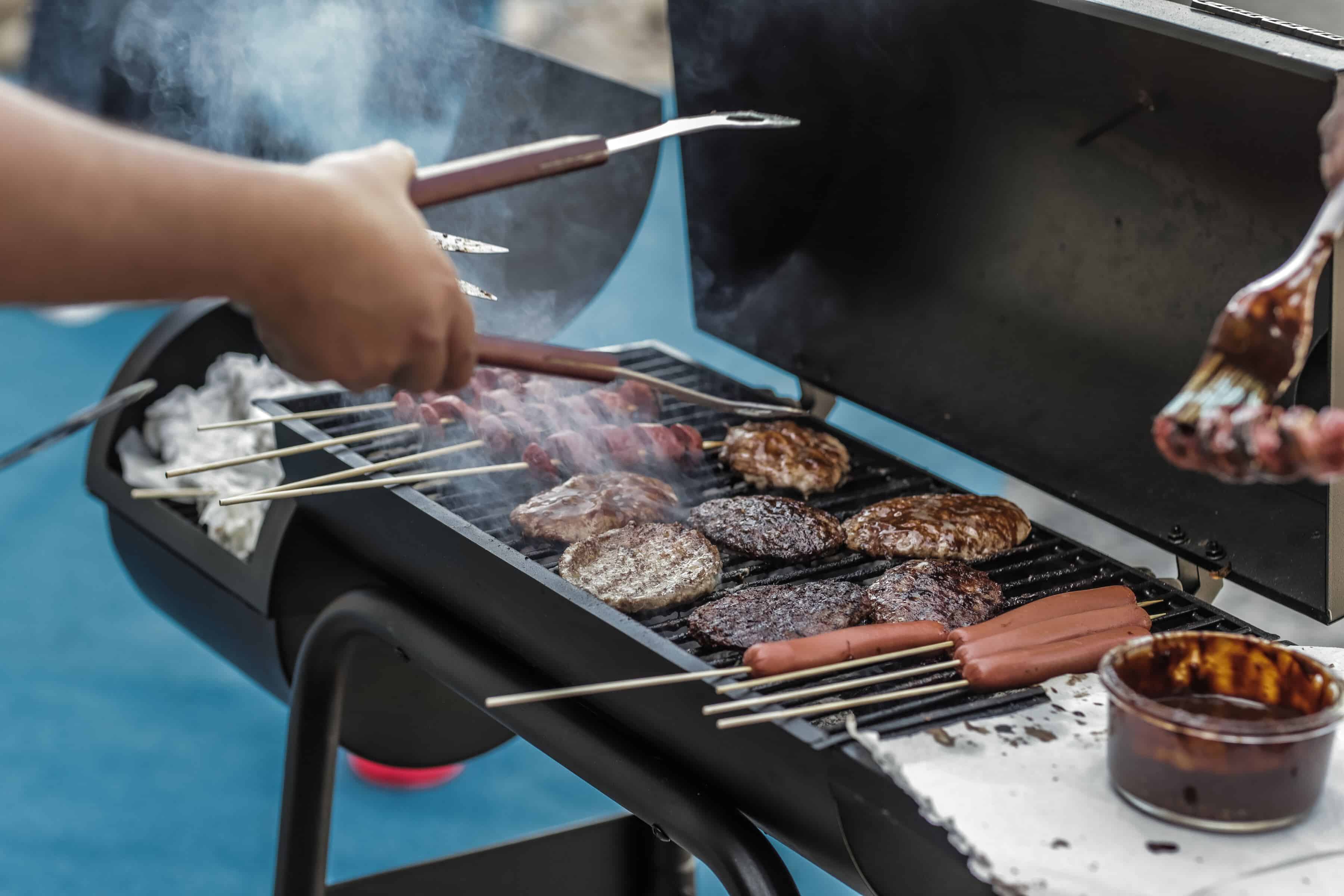 人がバーベキュースモーカーでソーセージと肉を焼いている