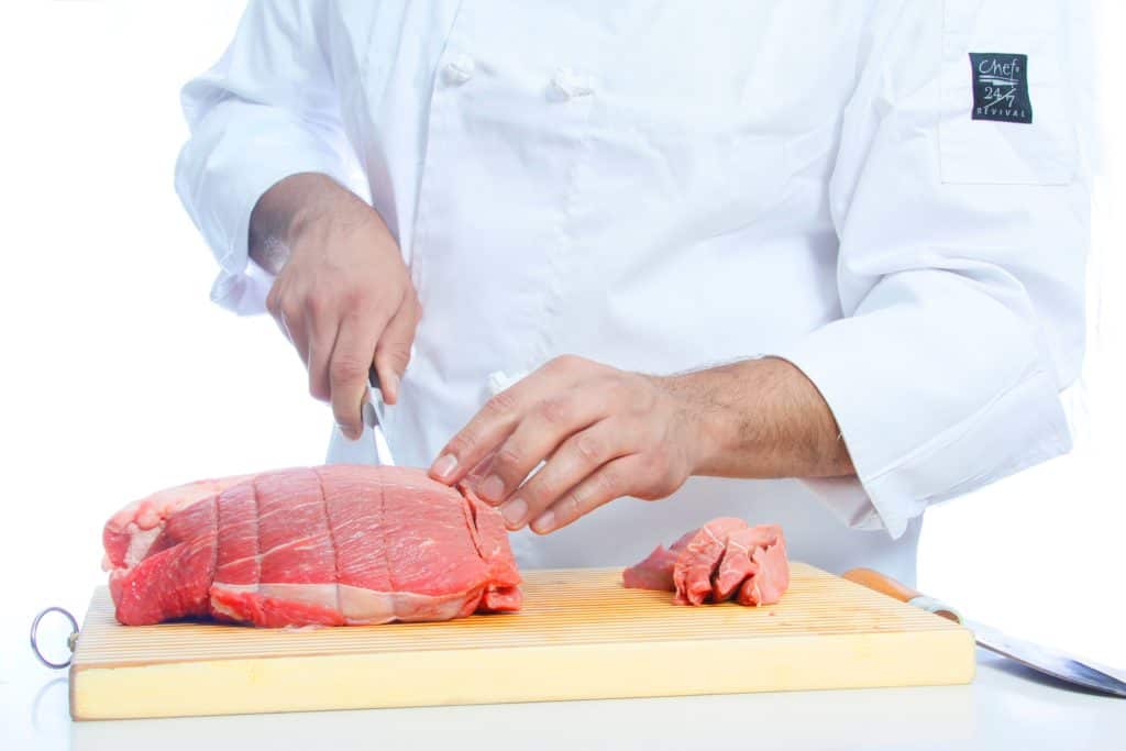 un chef coupe la viande avec un couteau