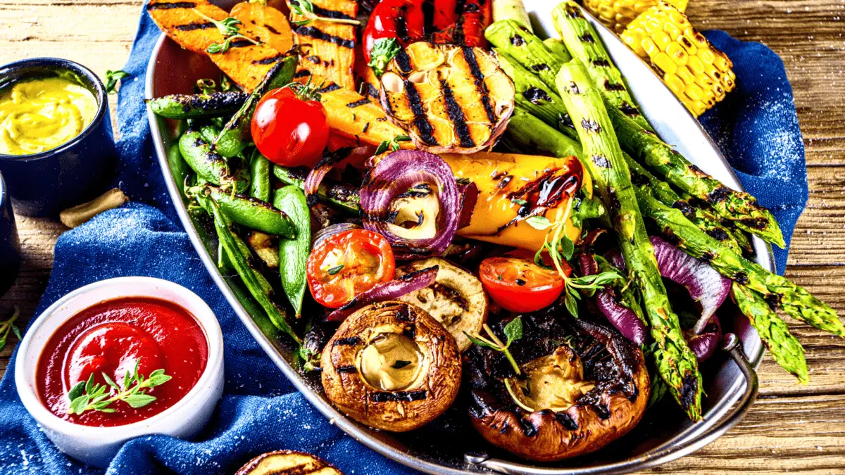 a plate of various grilled vegetables with sauces on the side