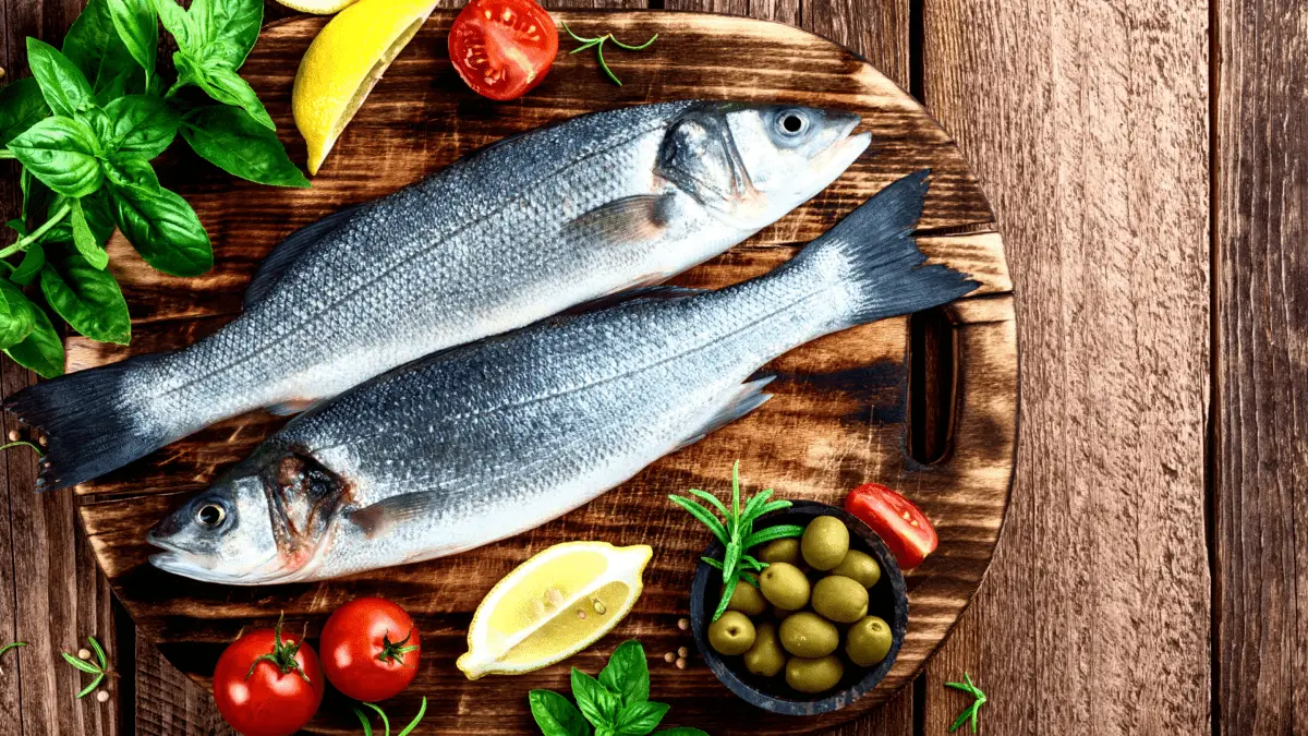 2 whole seabass on a wooden cutting board with surrounding herbs