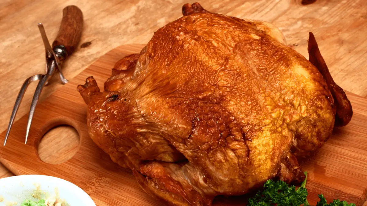 whole smoked chicken on a wooden cutting board with carving fork on the side